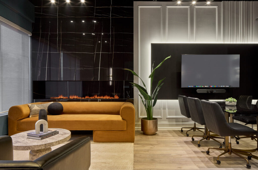 Modern office lounge with a mustard sofa, black marble fireplace, large plant, TV, conference table with black chairs, and marble coffee table—ideal as a stylish meeting room for small teams in Oakville with sleek decor and neutral colors. - Business Lounge Oakville